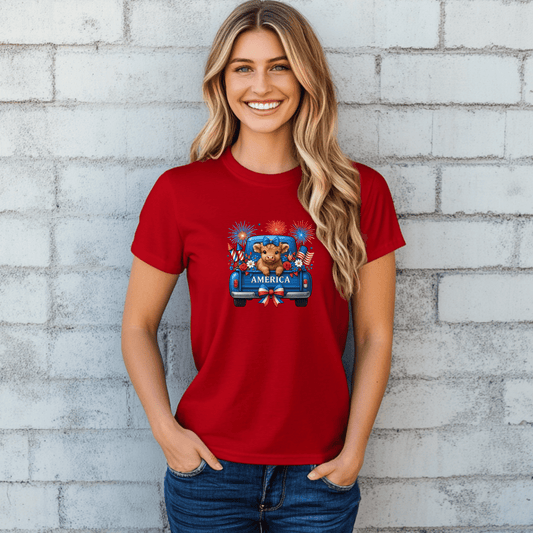 Woman wearing a red 4th of July t-shirt with highland cows in a blue truck, fireworks, and American flags — patriotic summer shirt for women.
