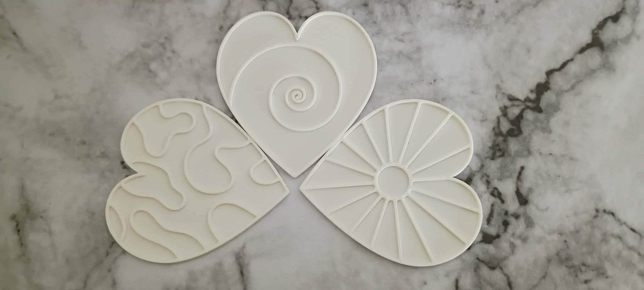 Set of four white ceramic coasters with decorative patterns on a marble surface