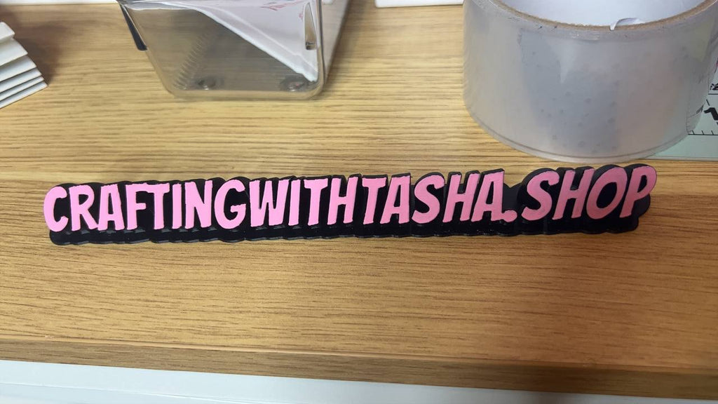 Pink wristband with 'CRAFTINGWITHTASHA.SHOP' text on a wooden surface