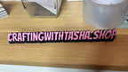 Pink wristband with 'CRAFTINGWITHTASHA.SHOP' text on a wooden surface