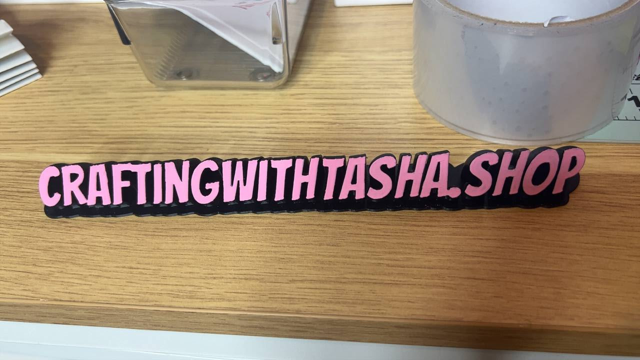 Pink wristband with 'CRAFTINGWITHTASHA.SHOP' text on a wooden surface