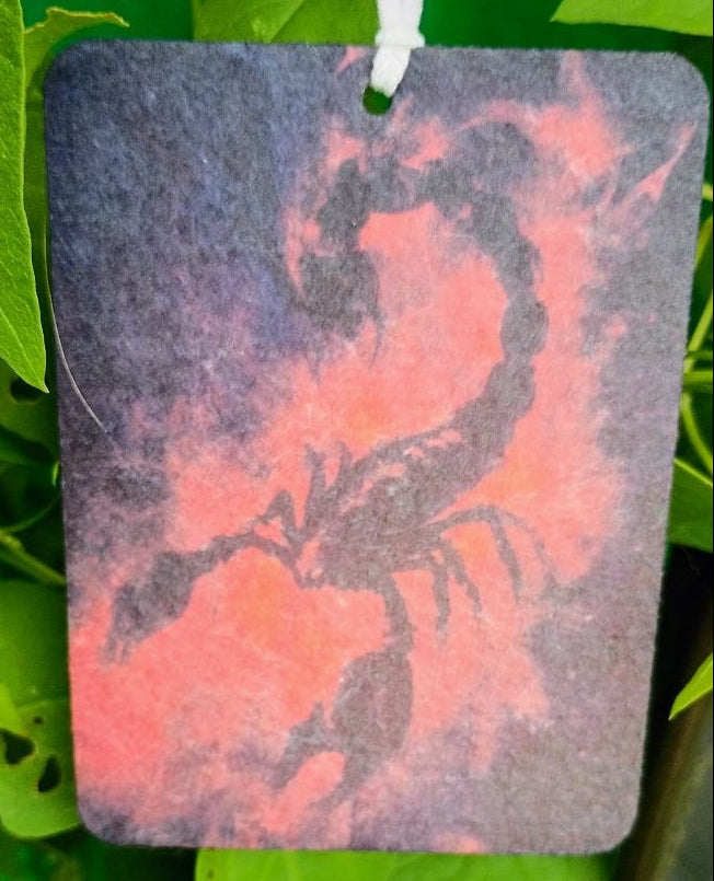 Decorative tag with a scorpion design hanging among green leaves
