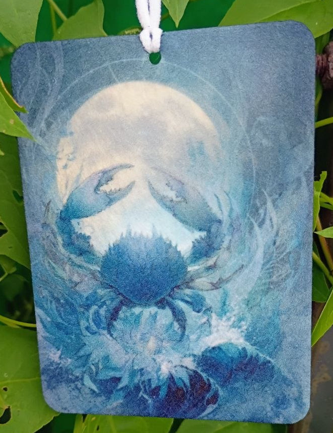 Decorative card with a blue and white design of a face and crab, placed among green leaves.