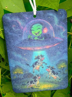 Colorful bag with cartoon design of a cow and alien spaceship hanging among green leaves.