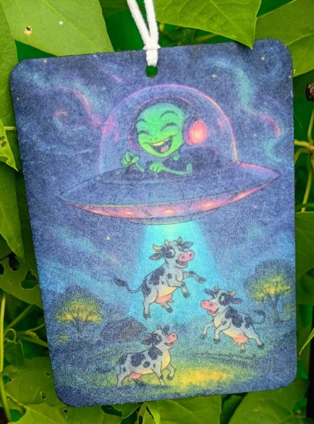 Colorful bag with cartoon design of a cow and alien spaceship hanging among green leaves.