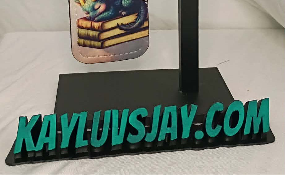 Keychain with dragon design on a stand with 'KAYLUVSJAY.COM' branding.